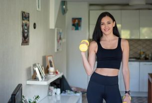 Smiling woman in activewear lifting dumbbells at home for a healthy lifestyle.